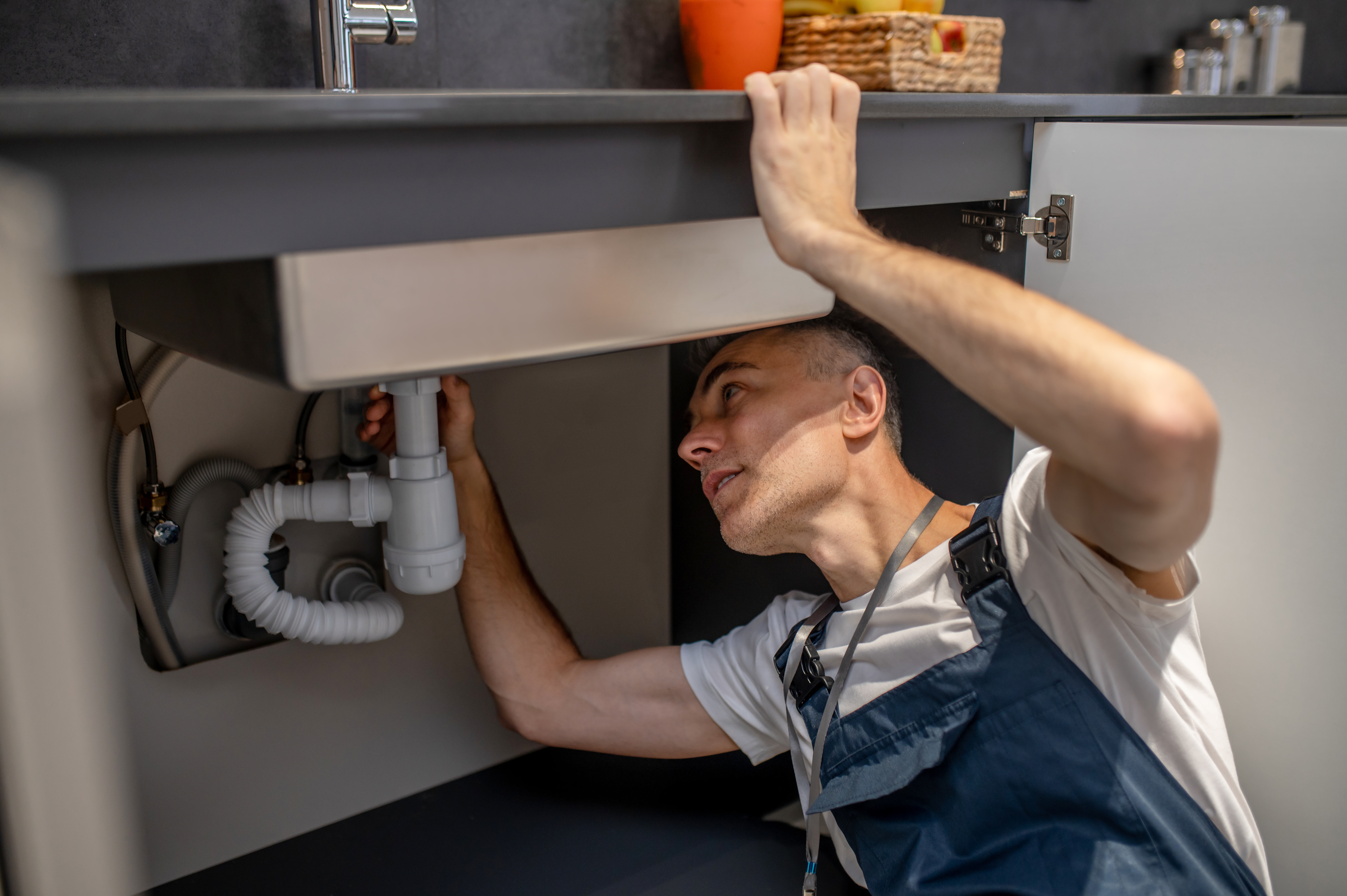Man carefully examining bottom of sink and pipe